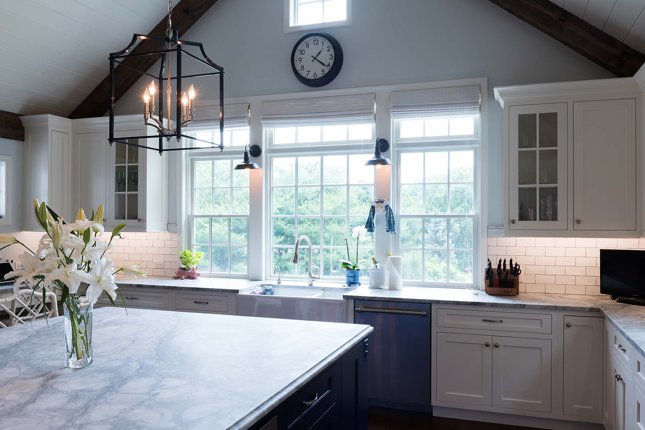 Bright kitchen with vaulted ceiling, white cabinets, and a large island adorned with fresh lilies and modern fixtures.