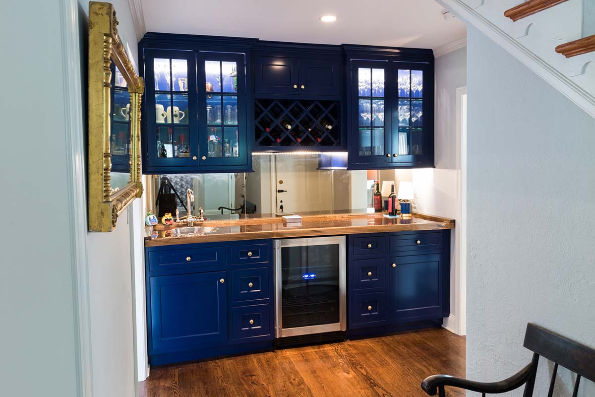 Stylish blue bar area with wine storage, glass cabinets, and a wooden countertop, nestled under a staircase.