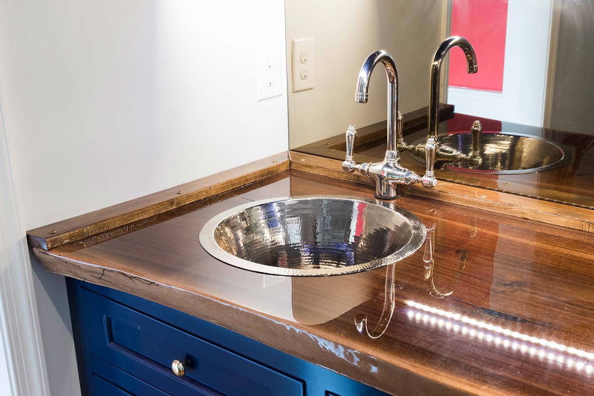 Elegant bathroom vanity with a wooden countertop, hammered metal sink, and blue cabinetry, illuminated by LED lights.