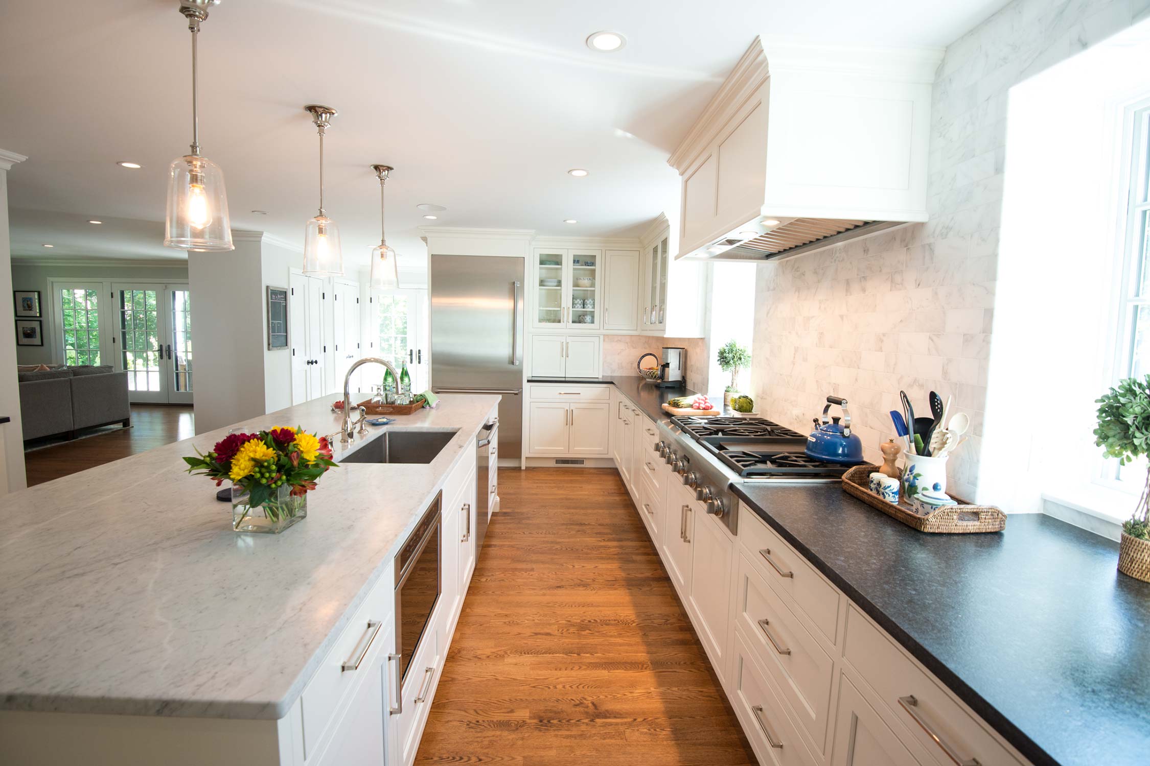 Elegant kitchen with marble island, vibrant floral centerpiece, white cabinets, stainless steel appliances, and hardwood floors under bright light.