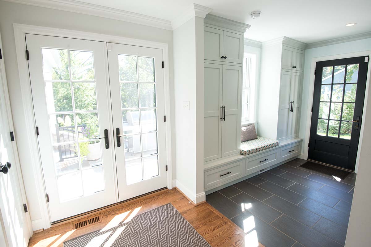 Bright entryway with white doors, built-in storage, window seat, and mix of hardwood and tile flooring under natural light.