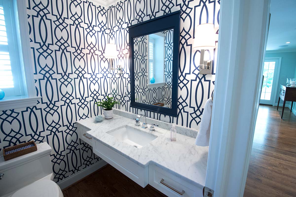 Stylish bathroom with blue geometric wallpaper, marble sink, modern mirror, and hardwood floor under bright natural light.