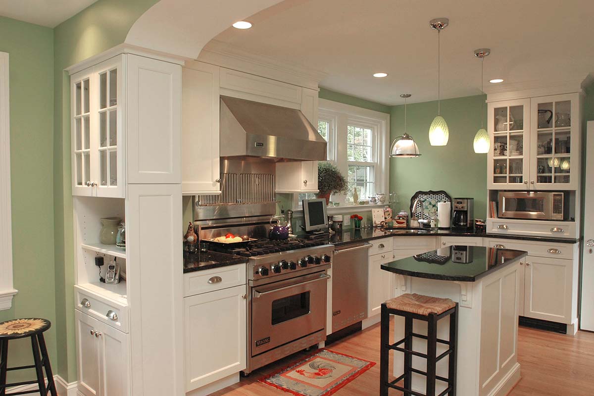 Cozy kitchen with green walls, white cabinets, black granite island, stainless steel appliances, and hardwood floors under warm lighting.
