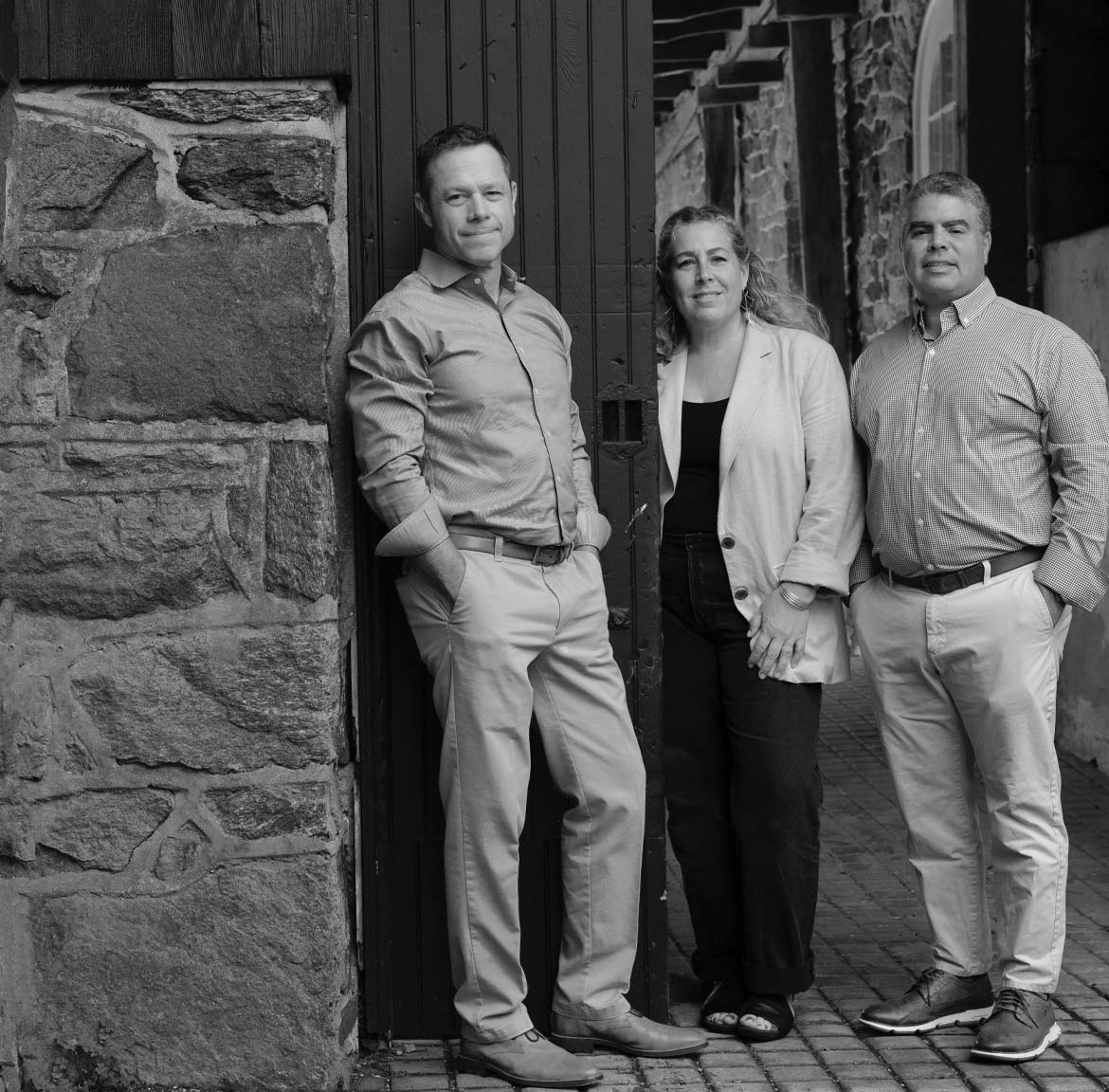 B&W photo of Andy Kerns, Gina Ranieri, and Greg Ranieri, Ranieri & Kerns founders, before a stone-facade home.