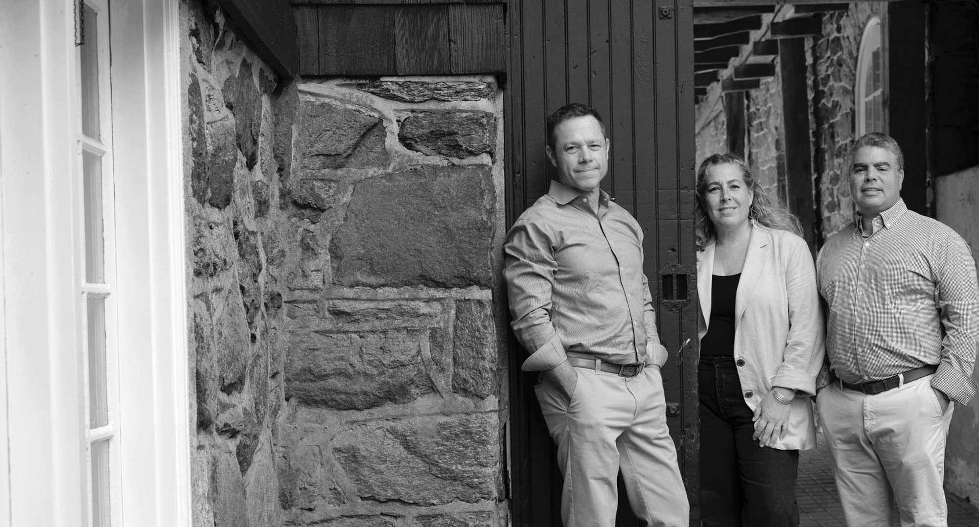 B&W photo of Andy Kerns, Gina Ranieri, and Greg Ranieri, Ranieri & Kerns founders, before a stone-facade home.