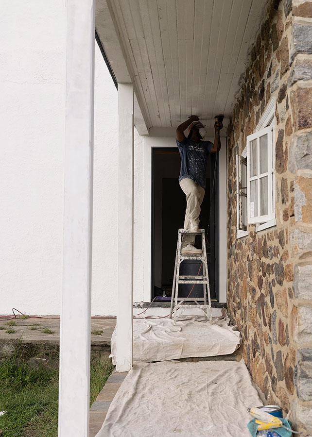 Painter on ladder painting historic home’s stone facade overhang.